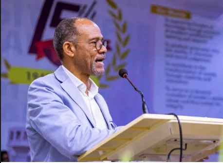 A speaker in a light blue jacket addressing the audience from a lectern.